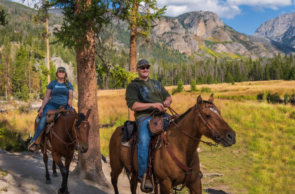Smiling young man and woman riding horses in the forest of Yellowstone National Park
