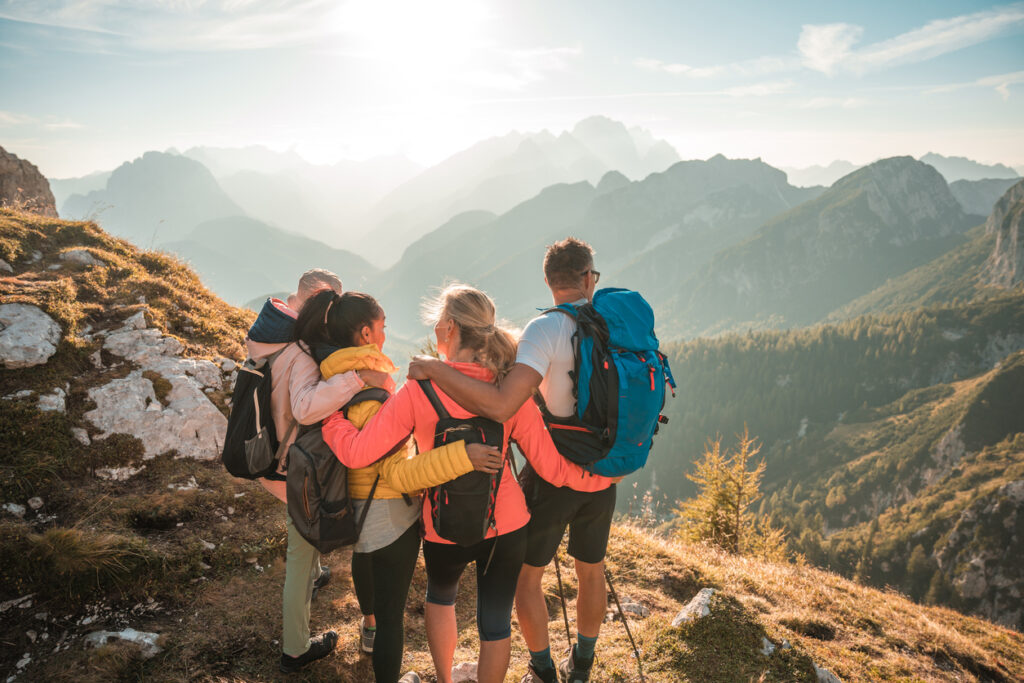 A diverse group embraces and has fun during their sunny day hike through the Julian Alps, taking in the beautiful views in the distance.