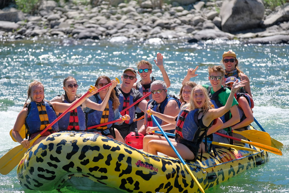 Adults smiling and waving from a yellow raft in class 1 rapids