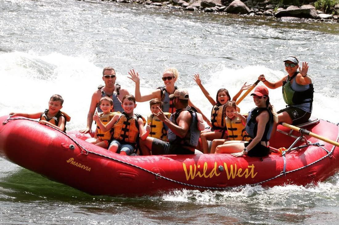 Adults and kids cheering from a red raft on the Yellowstone River.